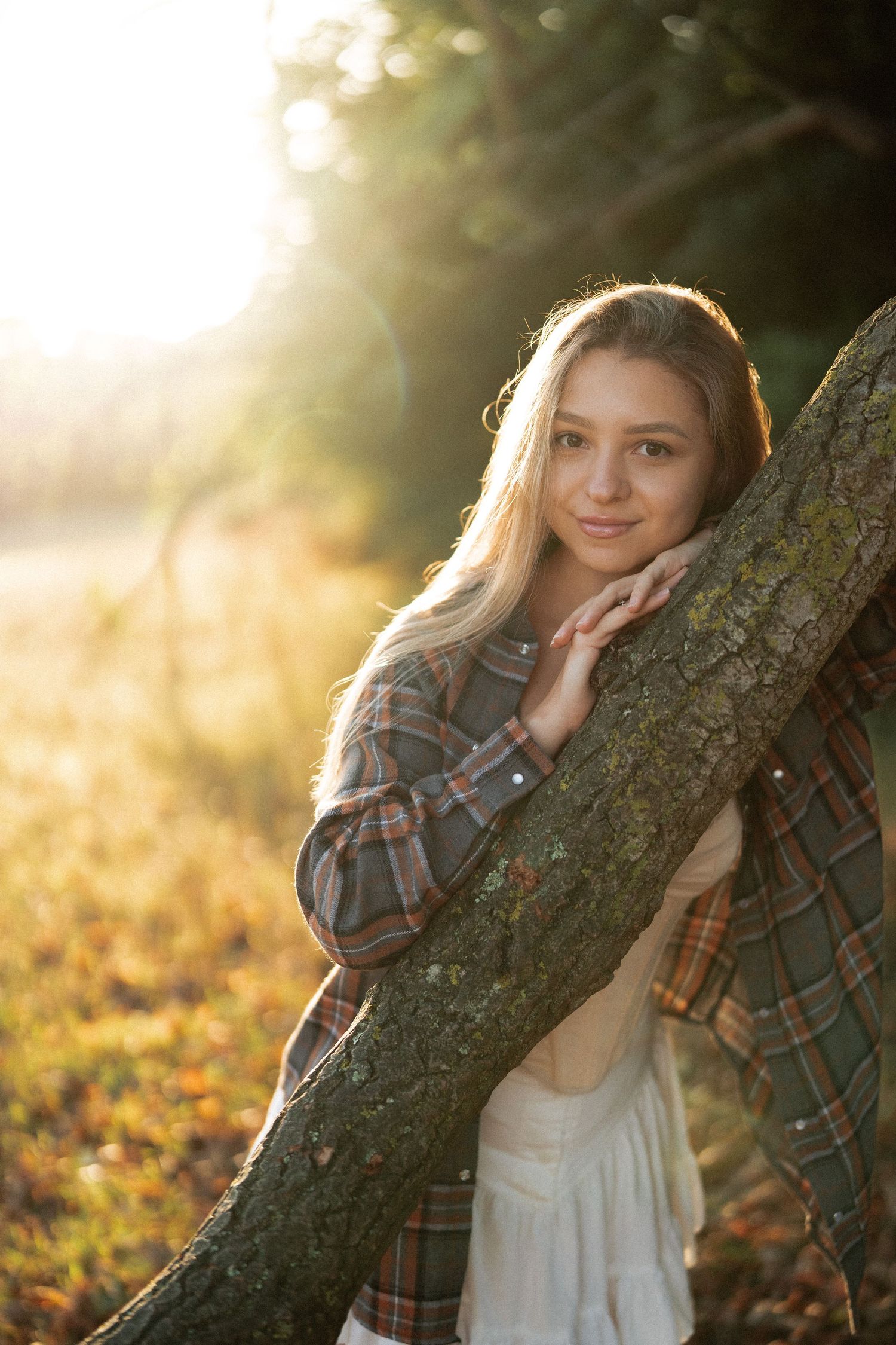 Portrait against tree trunk with warm sunset lighting filtering through leaves.