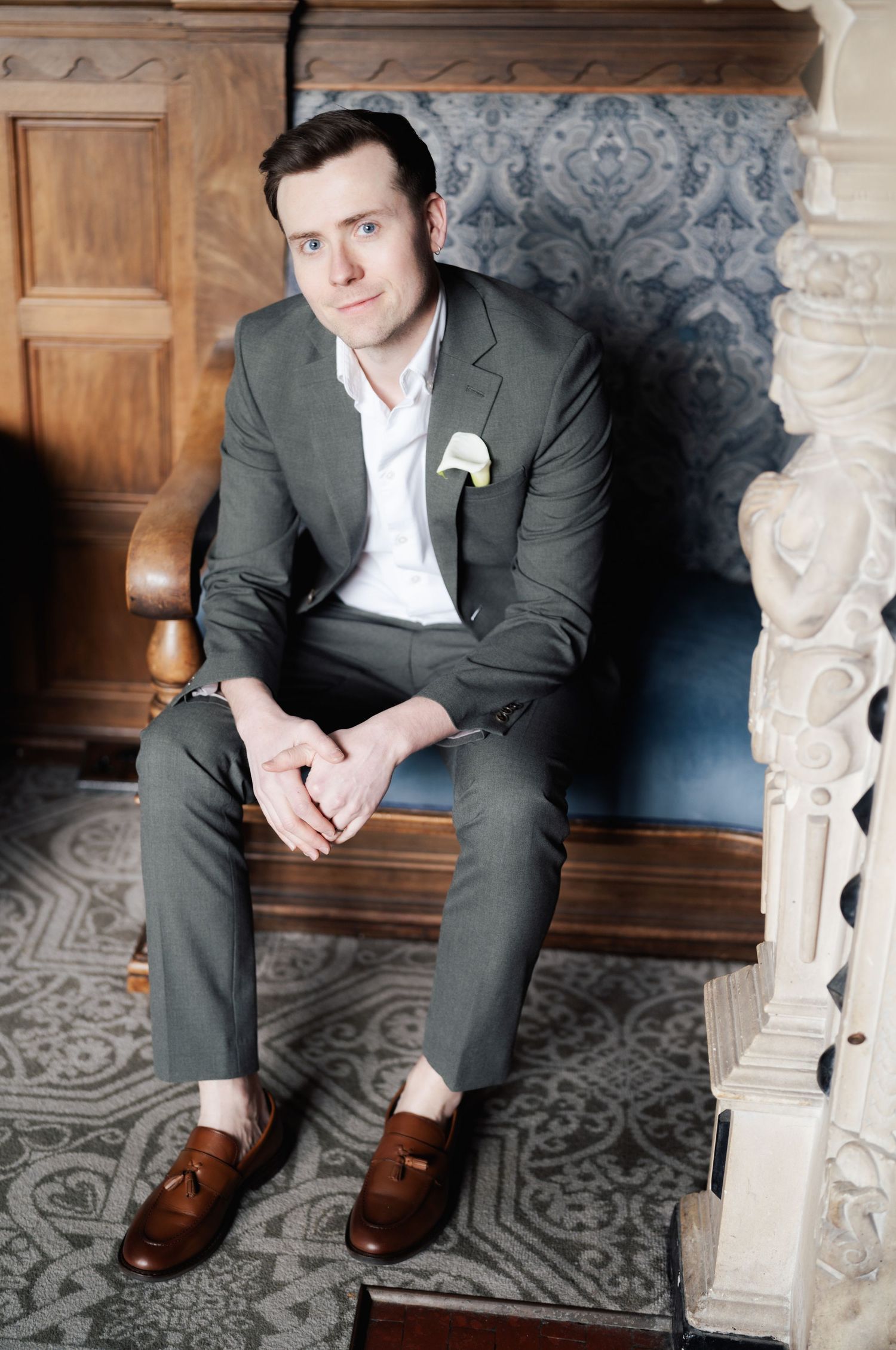 A person in a dark suit and white shirt sits on a decorative bench with patterned carpet and ornate architectural details.