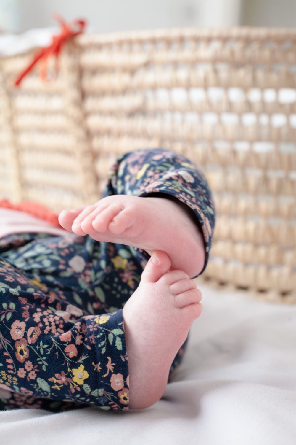 Close up of tiny baby feet wearing floral print pants in front of a woven moses basket