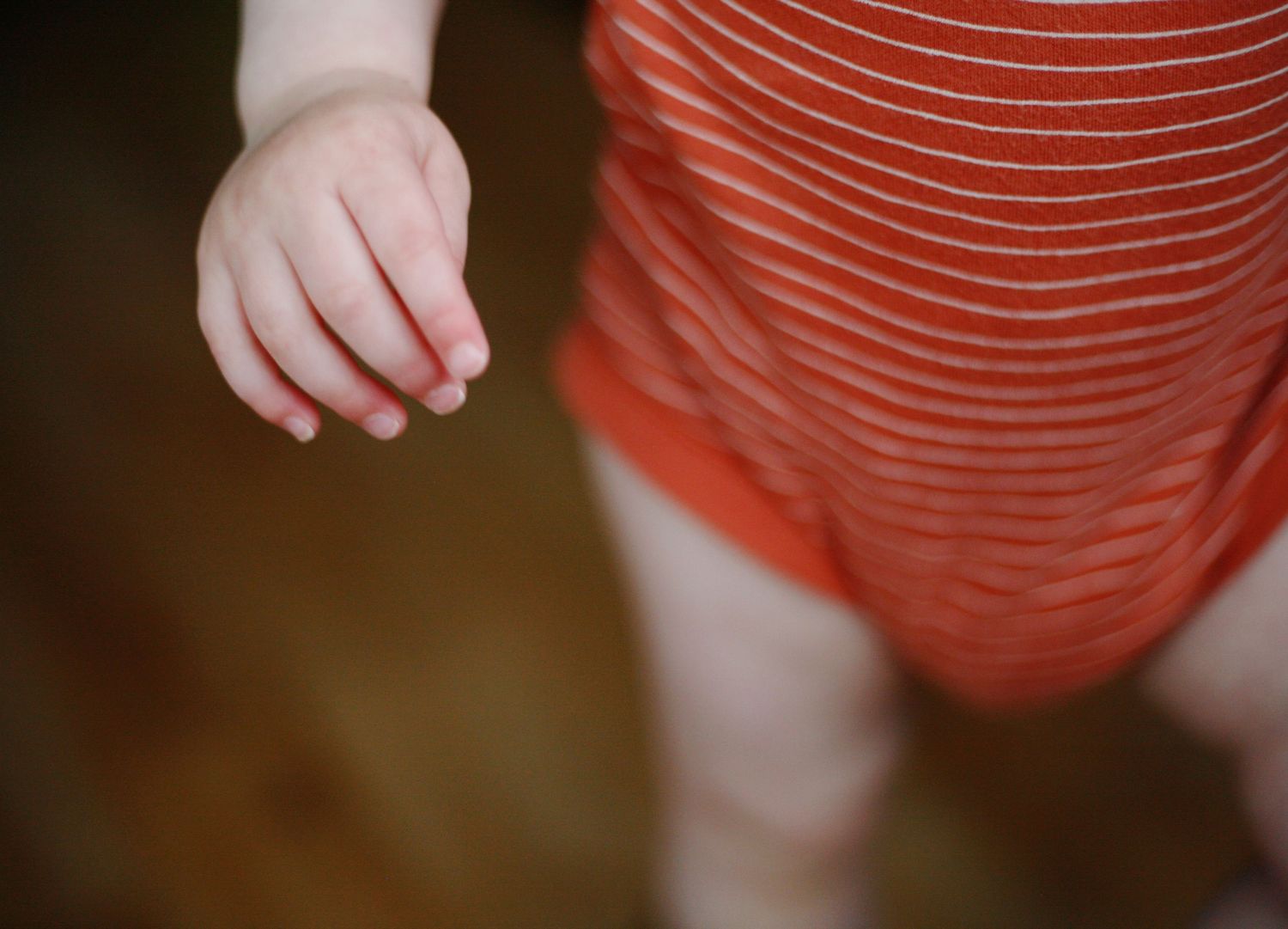 Close-up view of a small child's hand and red striped babygrow against a dark background.