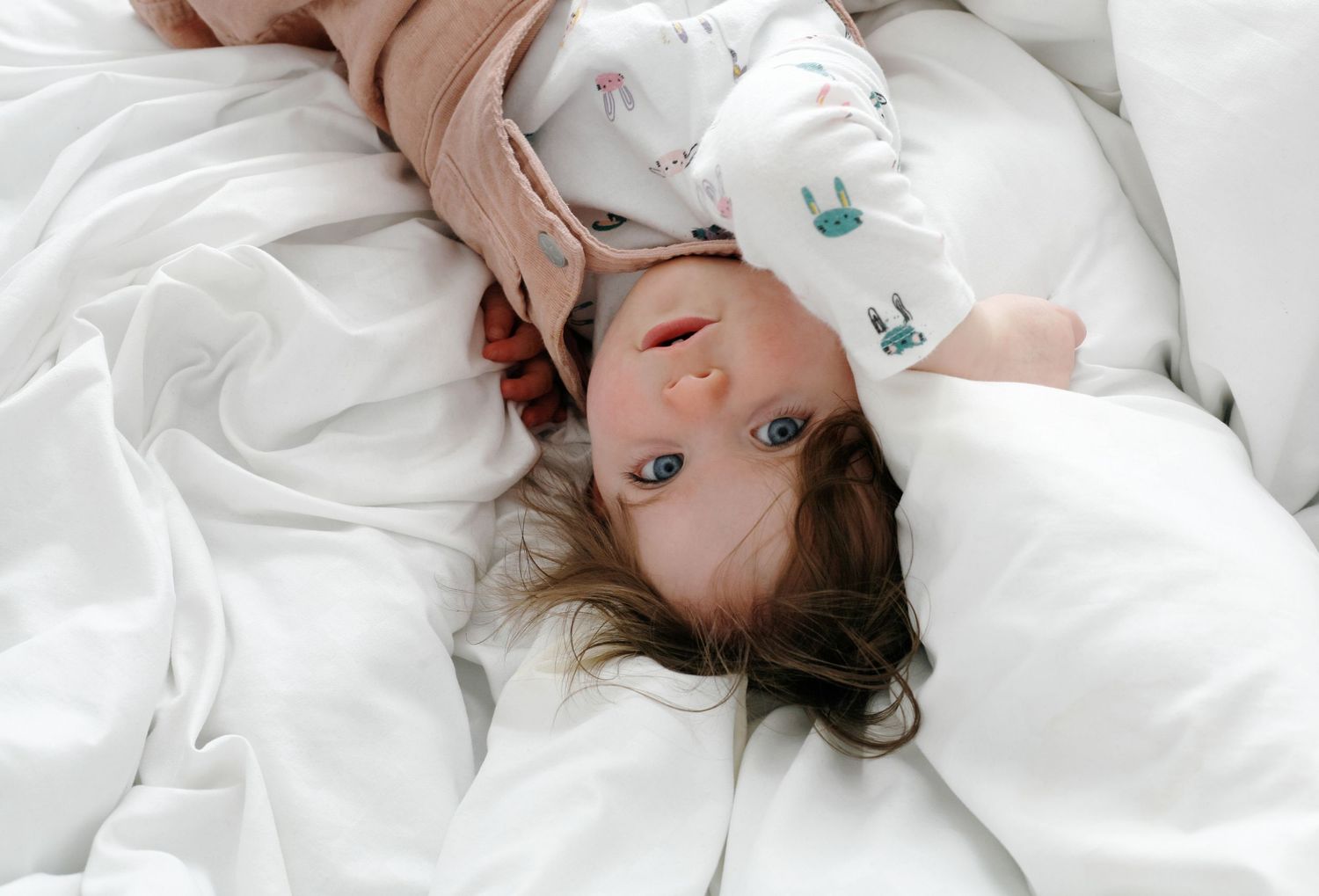 image showing a child in pink dungarees, captured in a natural moment on a soft white duvet