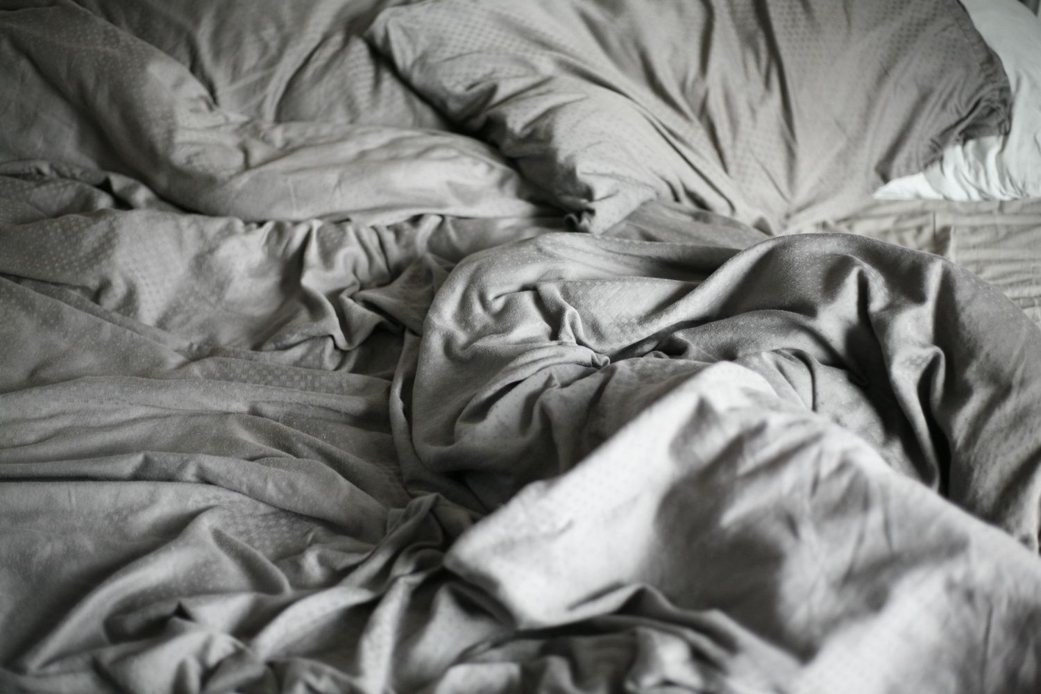 Rumpled and wrinkled grey bedsheets in a messy unmade bed.