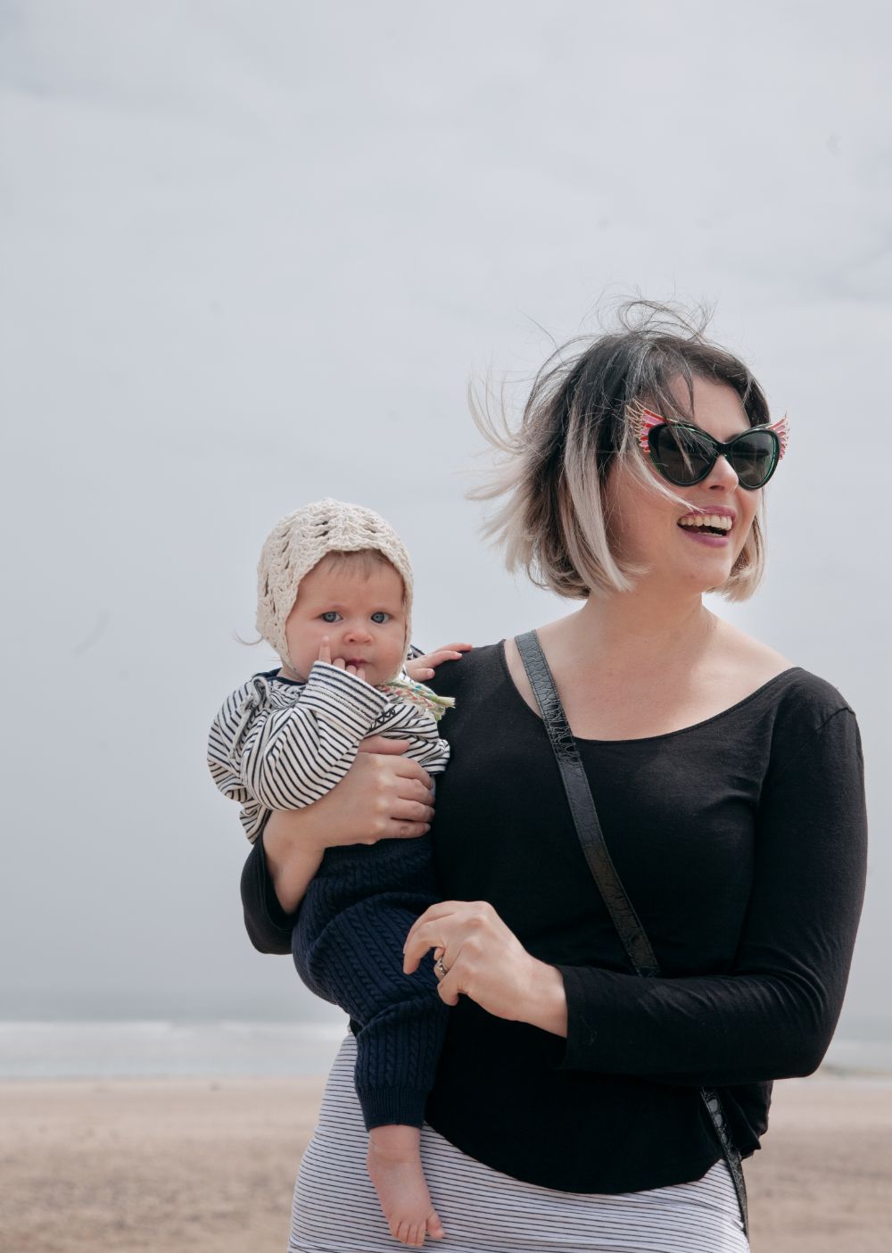 Mother and baby photographed at a beach location showing natural smiling expression and windswept hair