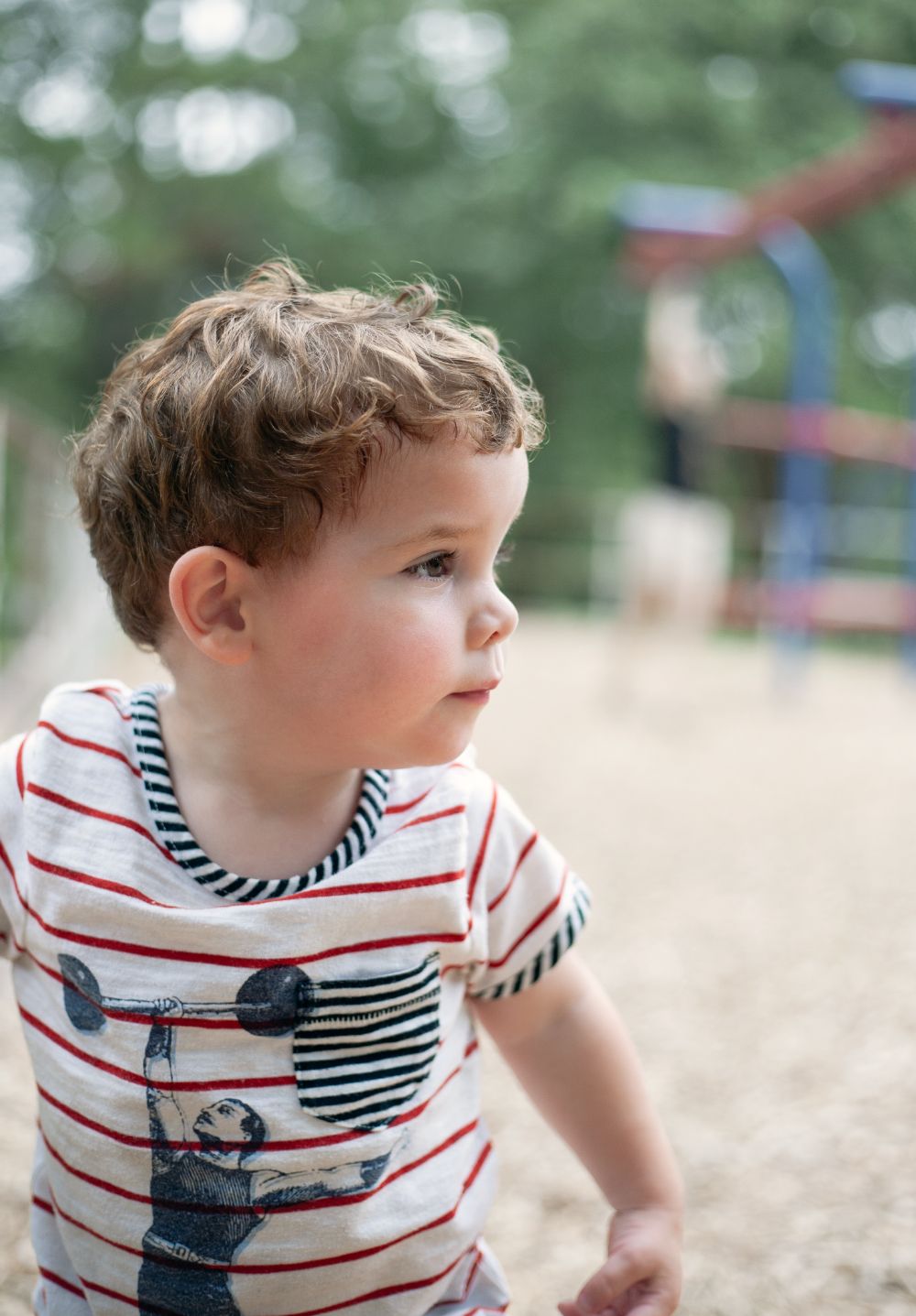 Child in striped nautical shirt playing in sandy area with playground apparatus int he background