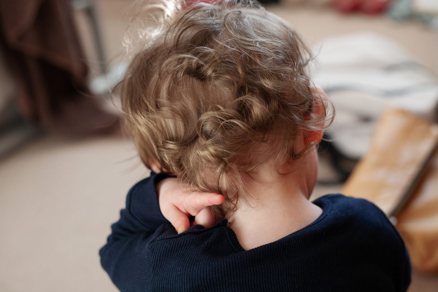 A small child pictured at home wearing a navy sweater with the image focussed on their lovely curls and a blurred messy background