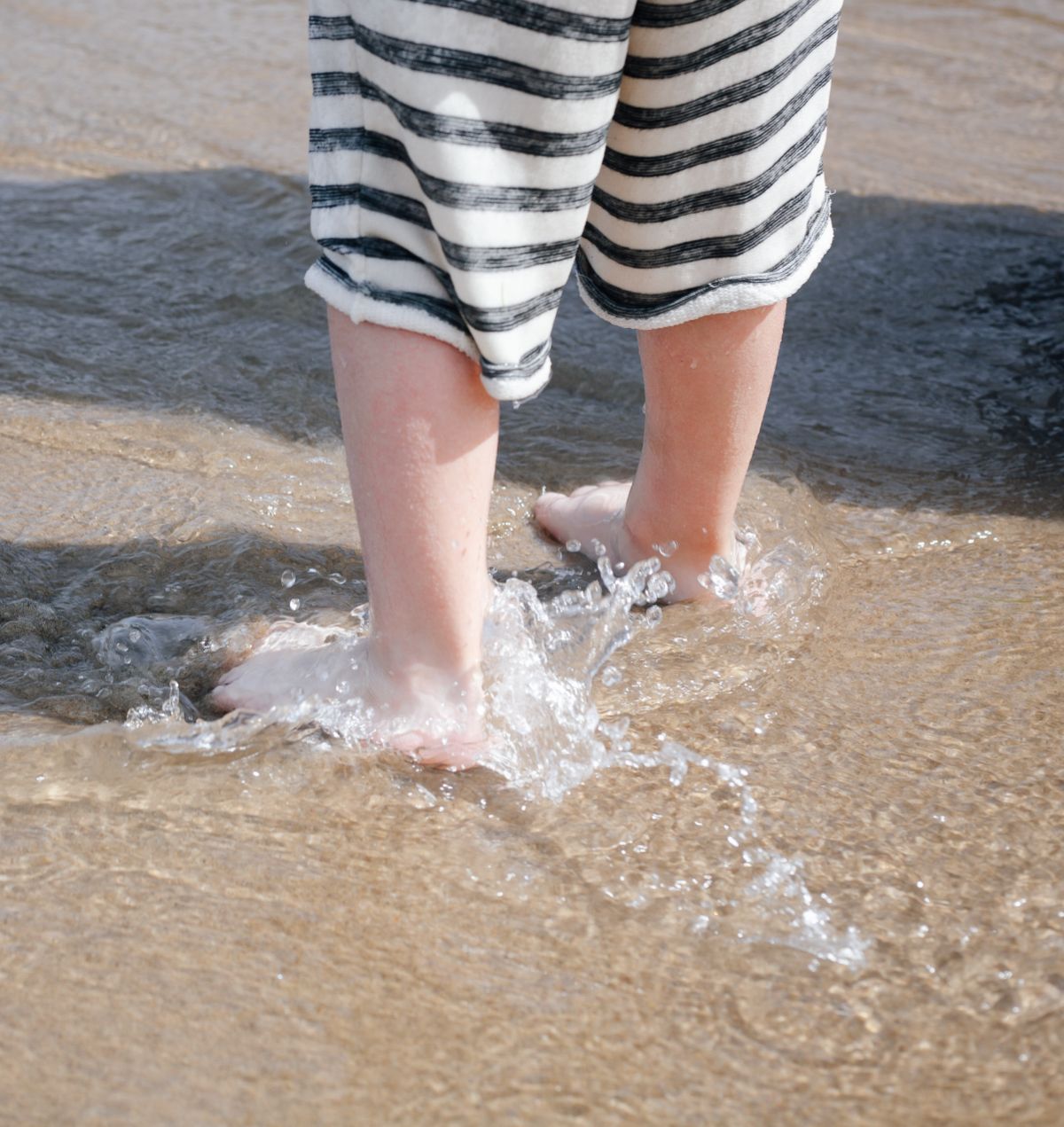 Striped shorts and feet splashing in ocean waves at the beach.