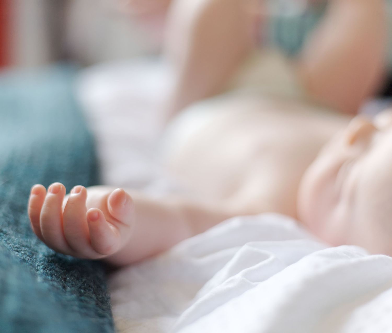 Close-up of small newborn baby fingers on a blanket in soft natural lighting.