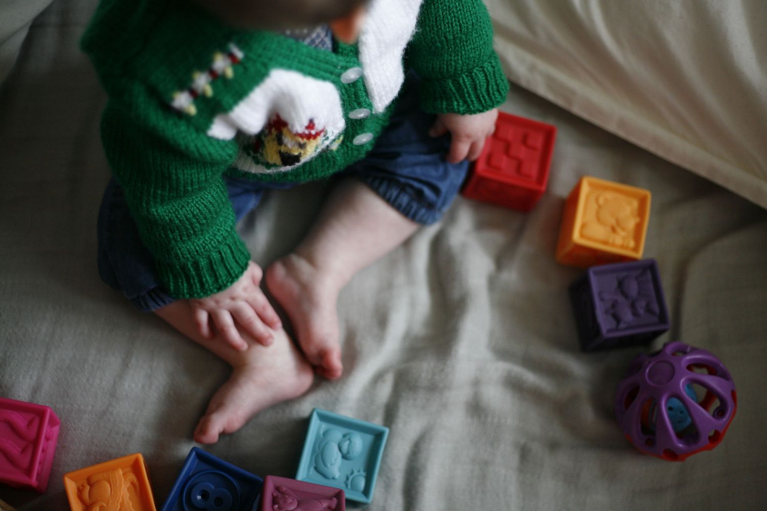 Close up view of baby hands and feet playing with colorful building blocks wearing a hand-knitted cardigan
