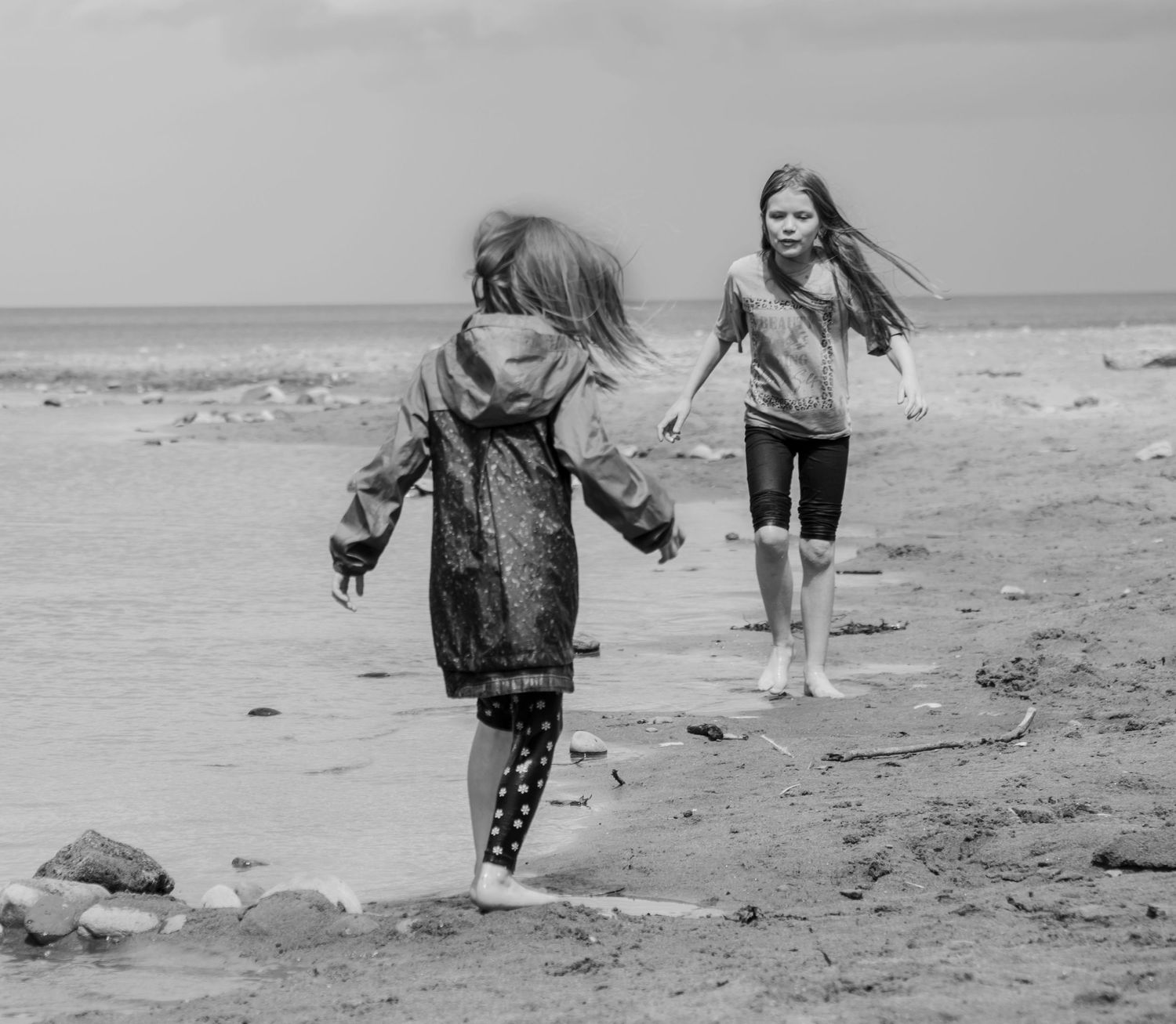 Black and white scene of two children exploring a rocky beach shoreline.