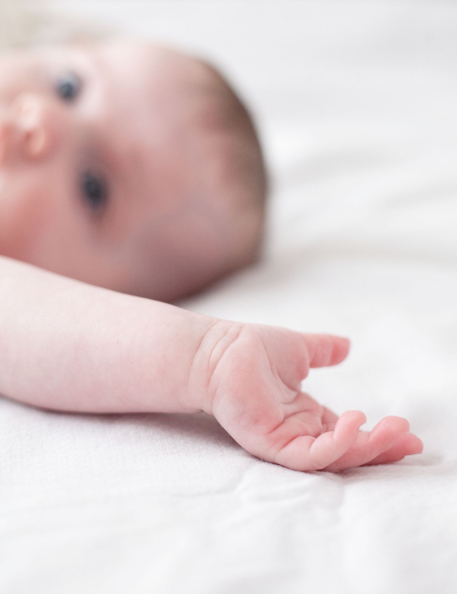 Closeup shot of a baby's tiny hand resting on white bedding with soft selective focus in natural light.