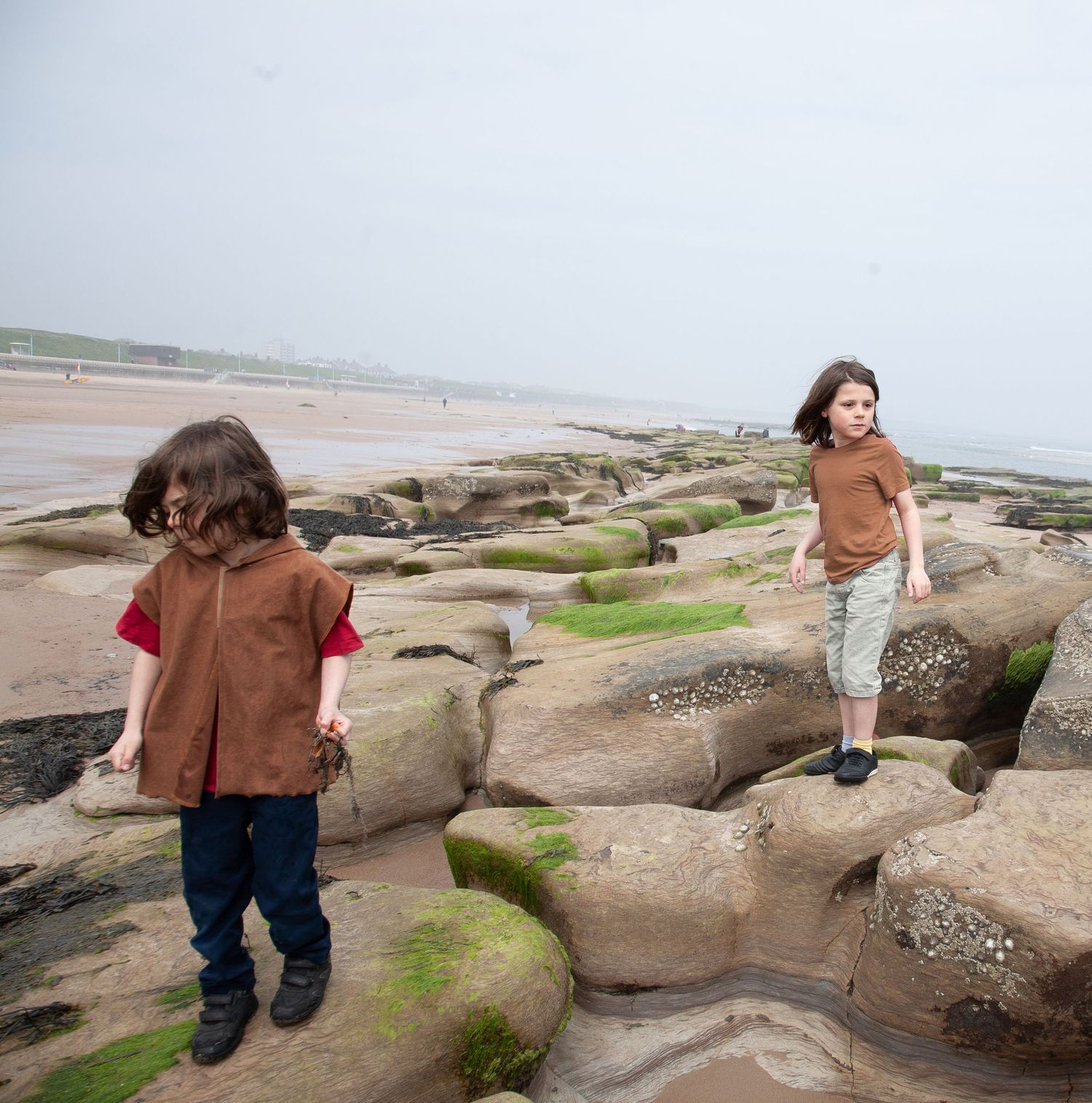 Two children at a beach location exploring rocky coastal terrain with moss-covered stones.