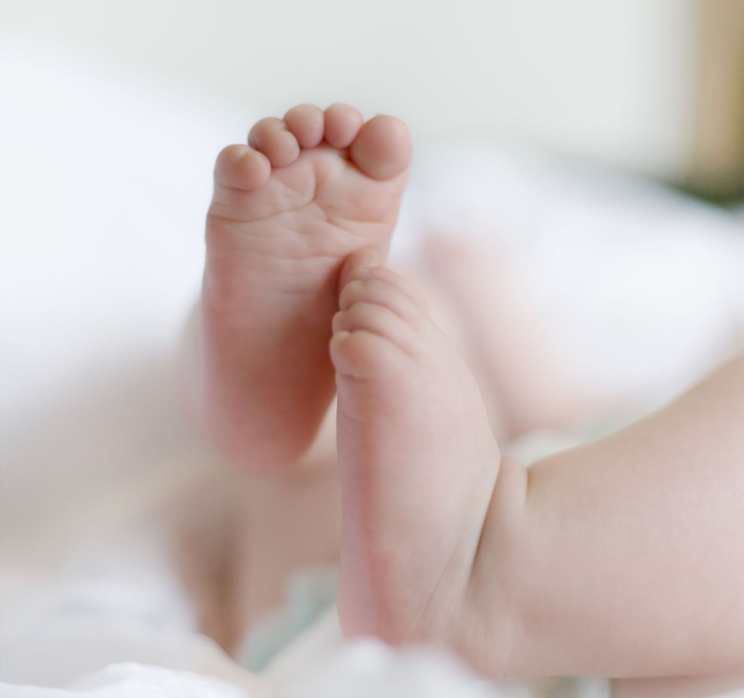 Tiny baby feet rest gently on soft white bedding in a hazy natural light.
