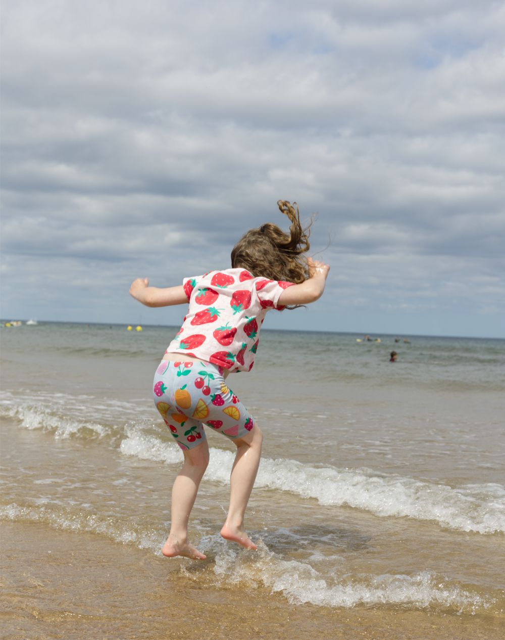 Location photograph showing a young child at the beach jumping and splashing in the waves