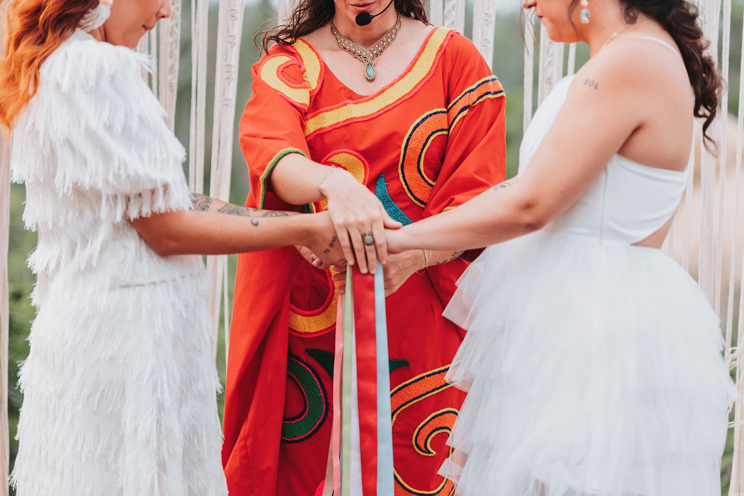 A bride in a white dress and person in red embrace during an emotional moment at a wedding ceremony.