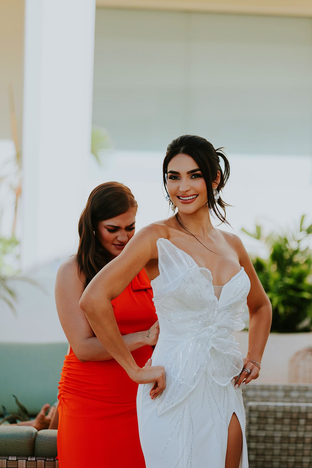 Bridesmaids in bright red dresses help adjust a white wedding gown in an outdoor setting.