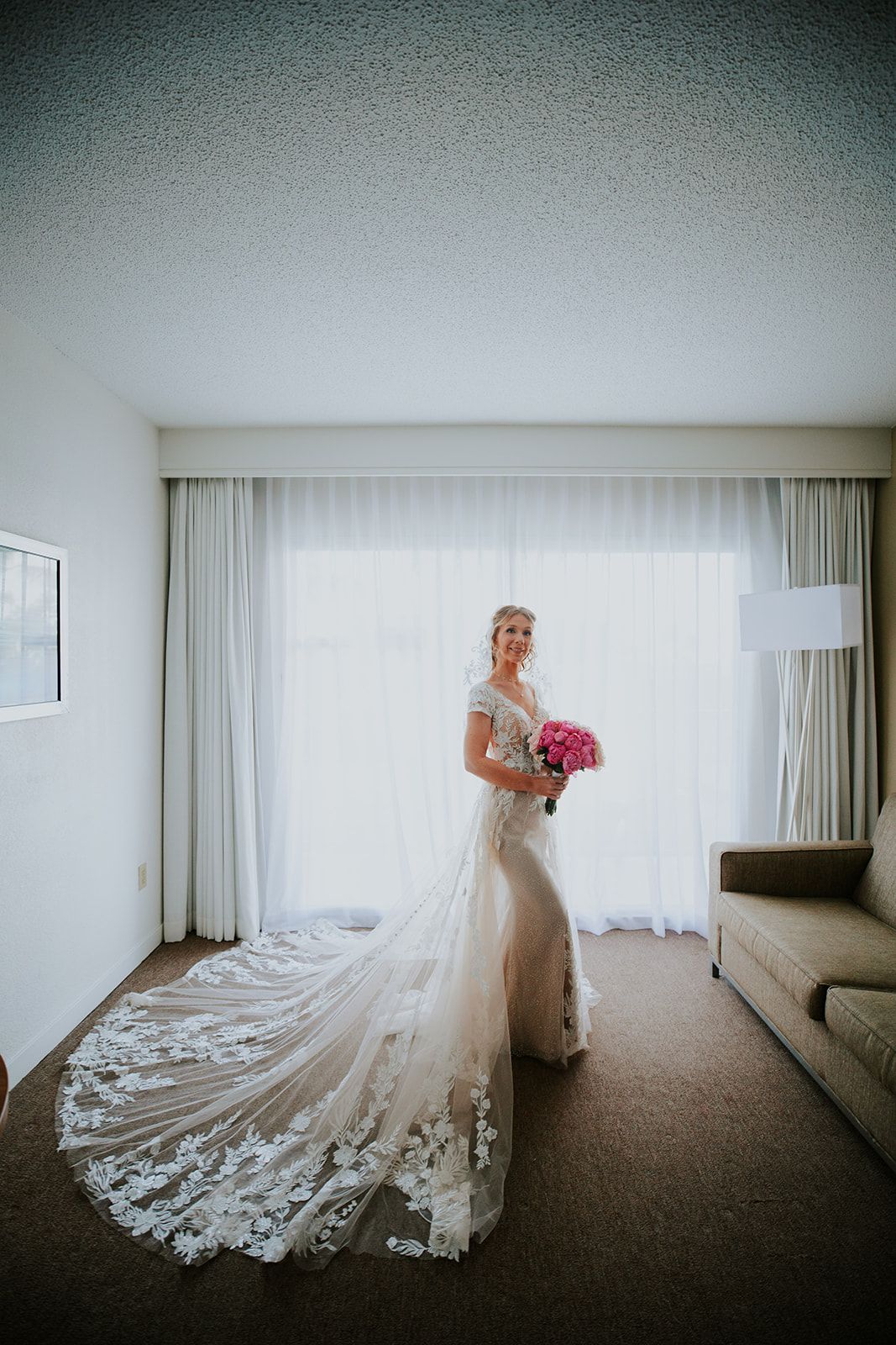 A wedding dress with a dramatic lace train flows across a neutral carpeted hotel room floor in a series of artistic shots.