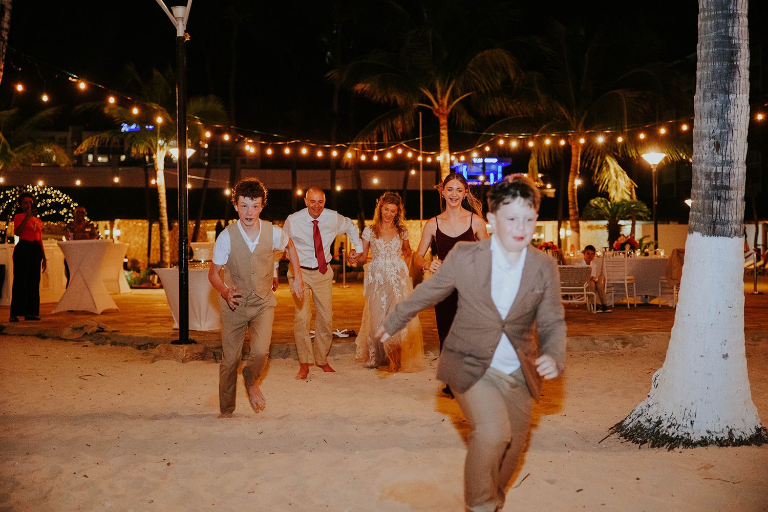 Wedding guests dance and celebrate at an outdoor evening reception with string lights overhead.