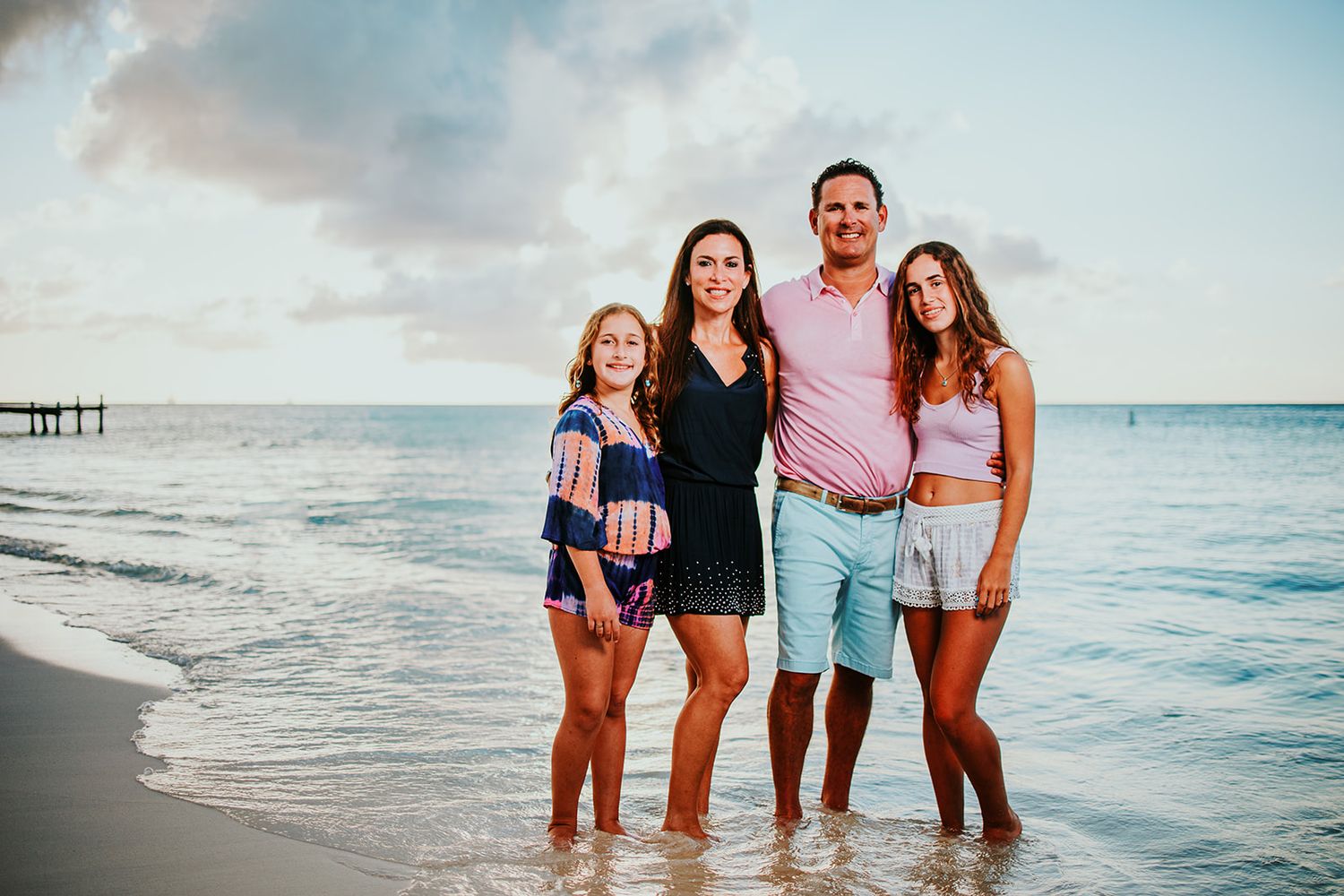 Family poses together on a tropical beach with crystal clear ocean waters in the background.