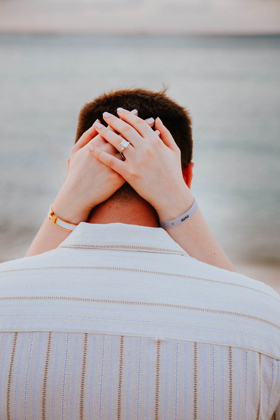 A person wearing a white shirt covers their face with hands in a sequence of three similar photos by the ocean.