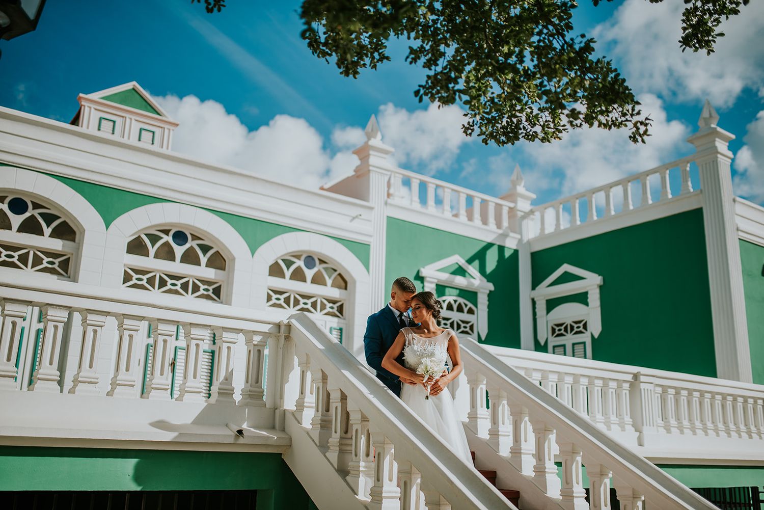 A vintage white colonial mansion with ornate architectural details and grand staircase provides an elegant backdrop.