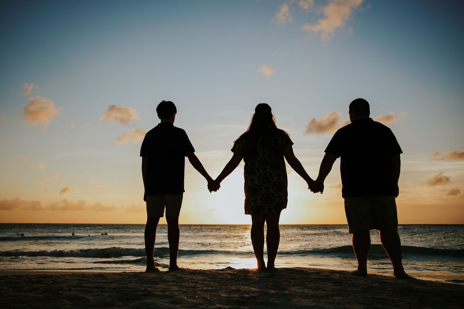 Silhouettes of people holding hands against a dramatic sunset sky at the beach.