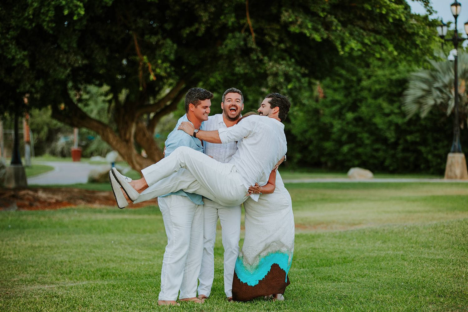 A group in matching white outfits poses playfully on a lush green lawn during a sunny outdoor photo session.