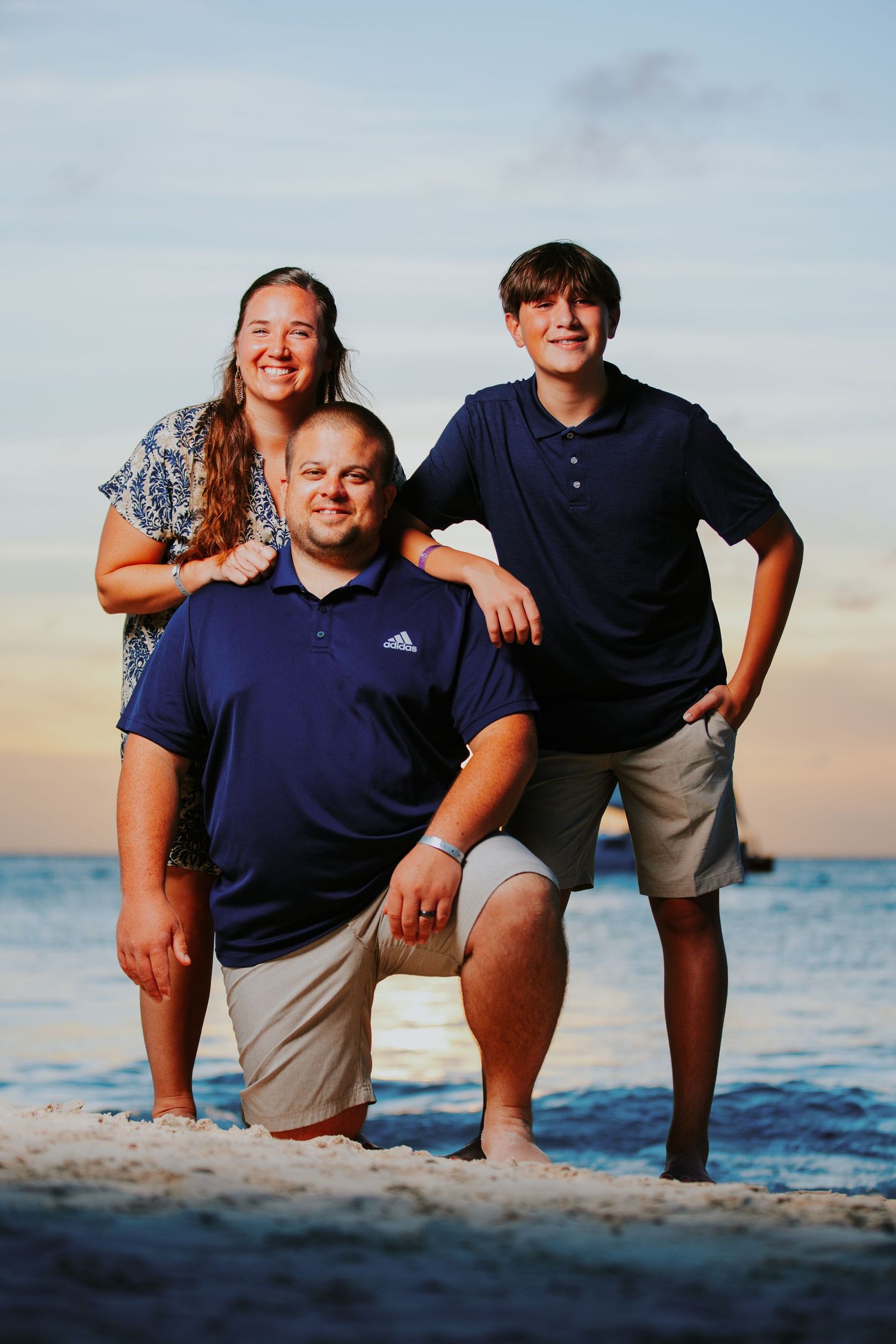 A family poses together on a beach at sunset with the ocean waves visible in the background.