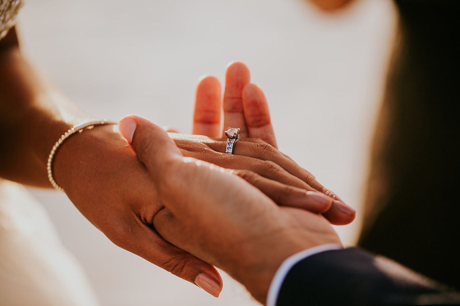 Close-up shot of hands exchanging a diamond engagement ring in warm lighting.