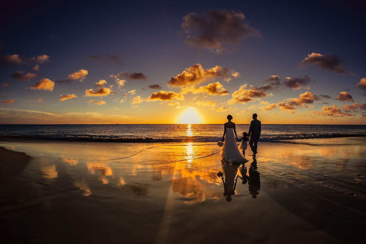 Stunning panoramic beach sunset with silhouettes reflected on wet sand.