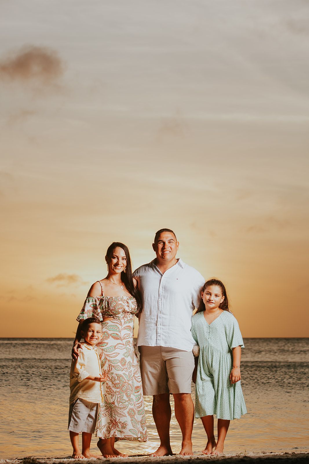 Family poses together on a beach at sunset with the ocean in the background.