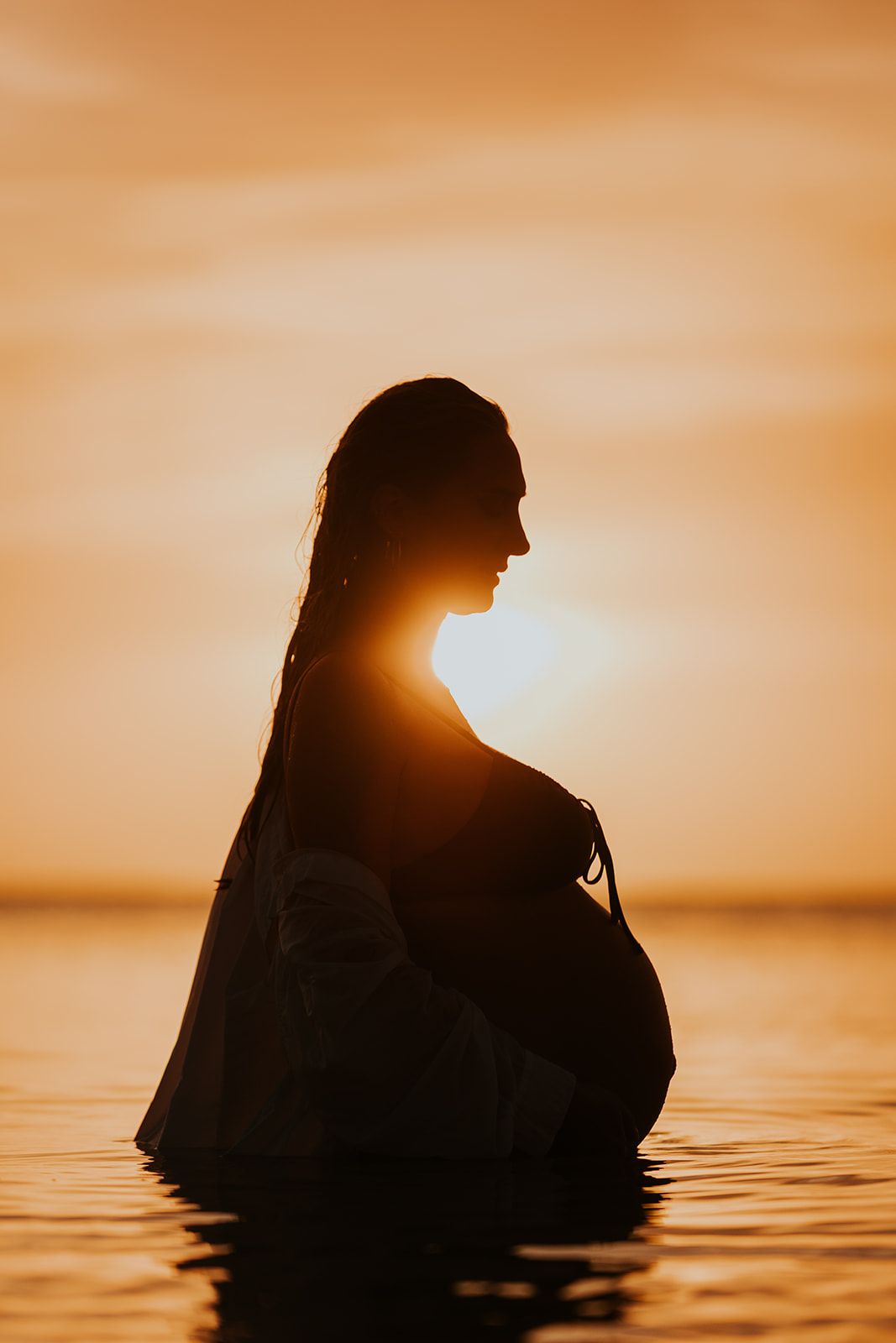 Silhouette of figure in water against vibrant orange sunset sky.