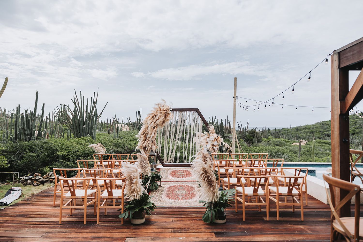 Rustic outdoor wedding venue setup with wooden benches and string lights under cloudy skies.