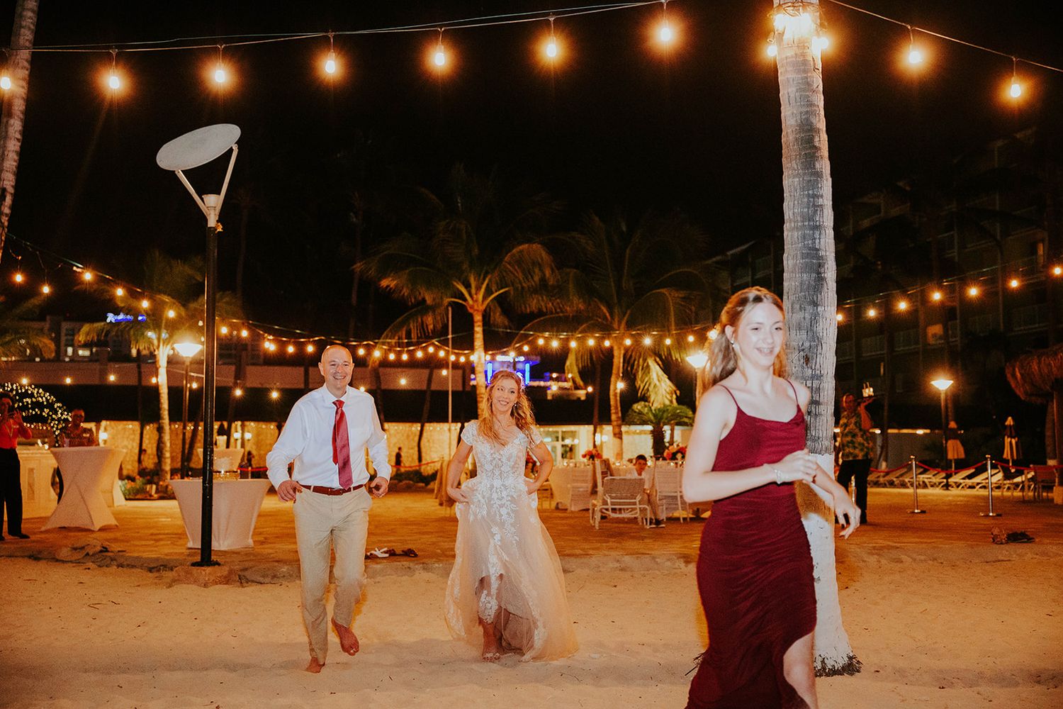 String lights illuminate an outdoor evening event with guests mingling and dancing at a festive celebration.