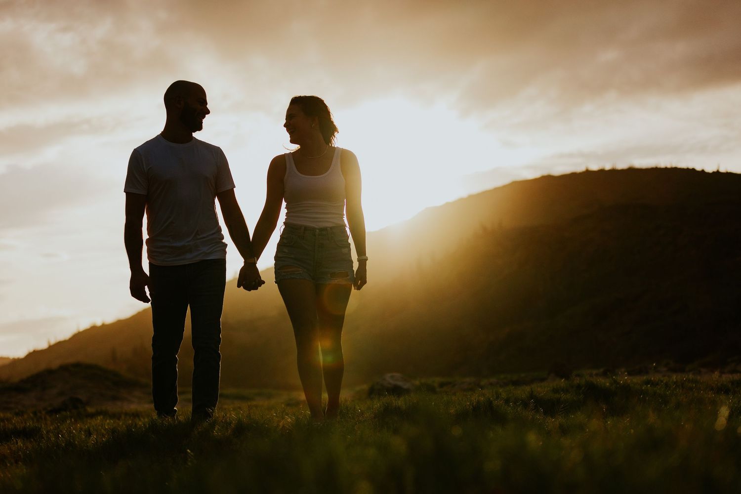 Silhouette of couple walking along mountain ridge during sunset.