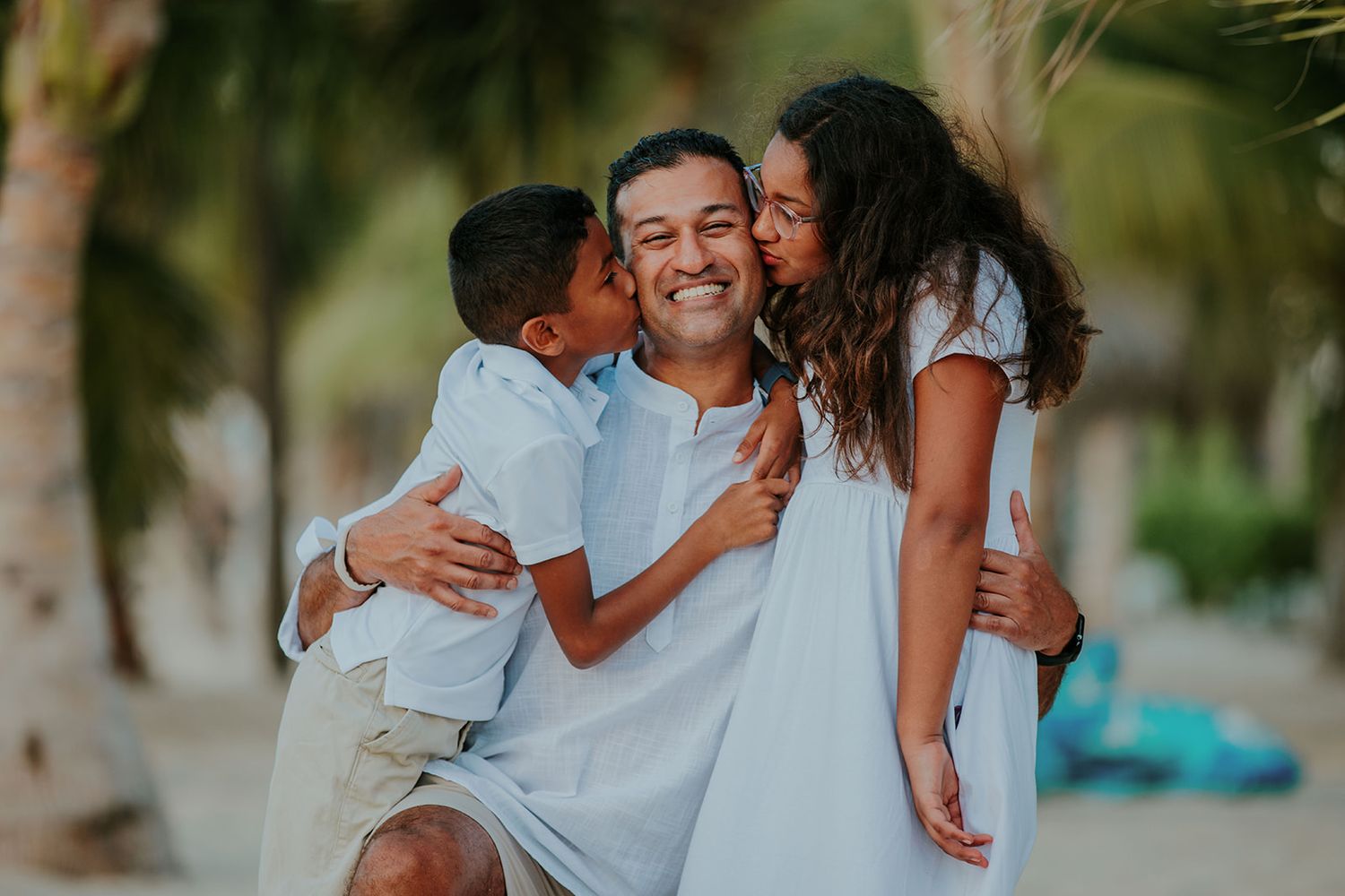 A family wearing white clothes embraces and laughs together during an outdoor photo session in a natural setting.