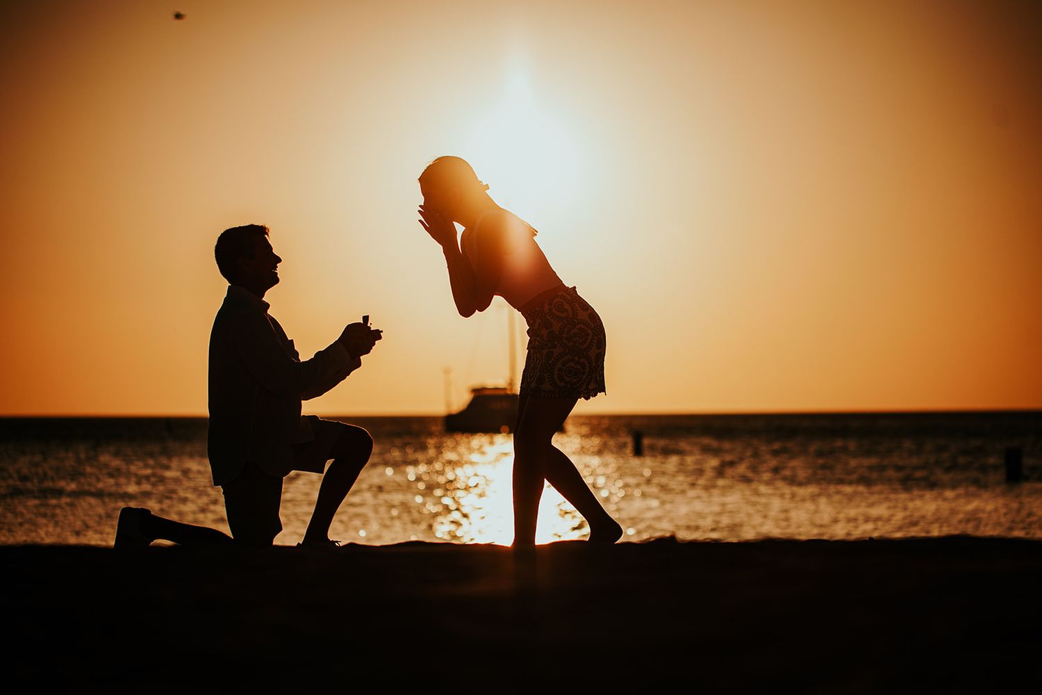 Silhouettes of proposal moment on beach at sunset.