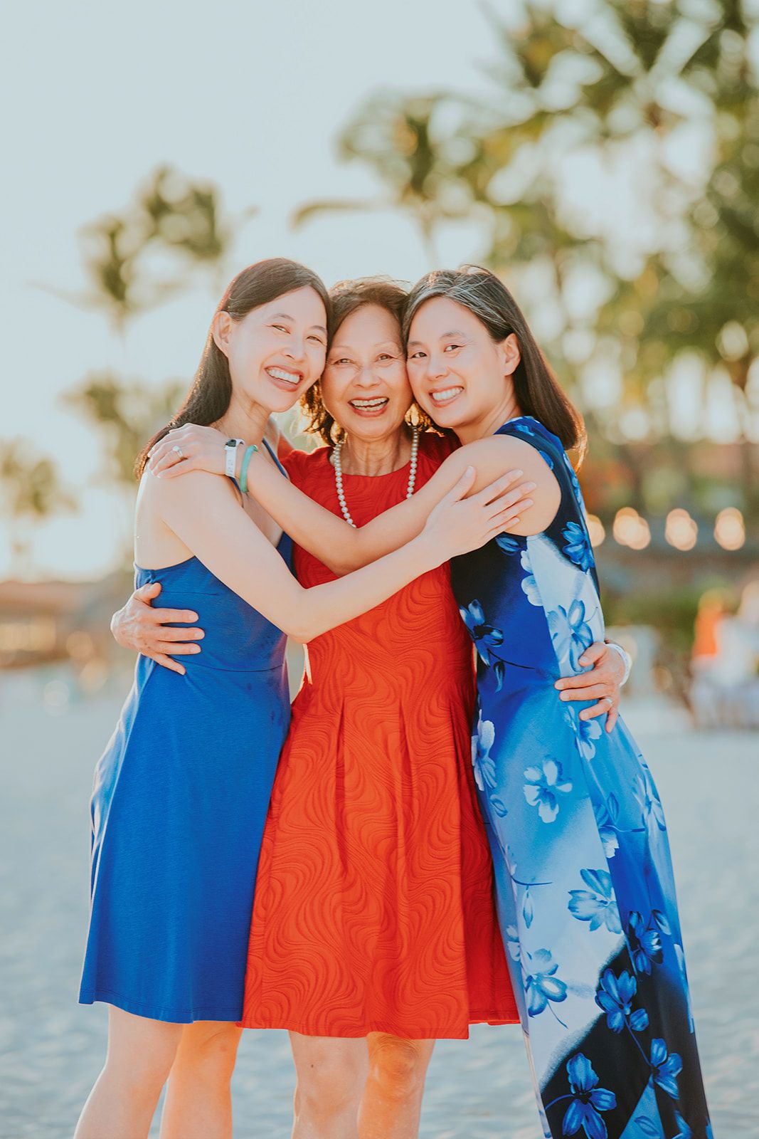 Three friends in coordinating blue and orange dresses pose together on a beach at sunset.