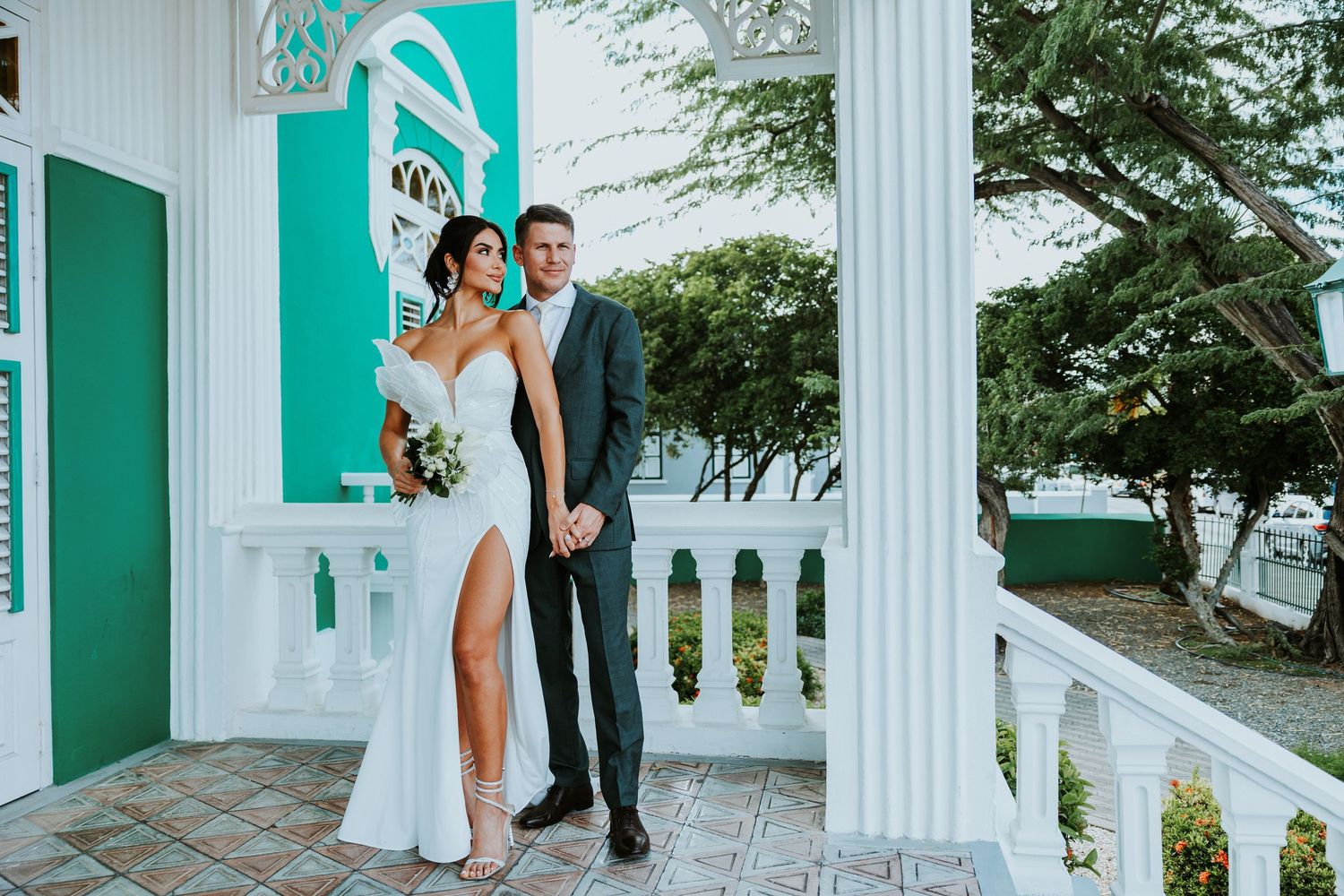 Wedding couple shares romantic moments in front of white columns with turquoise accents at a tropical venue.