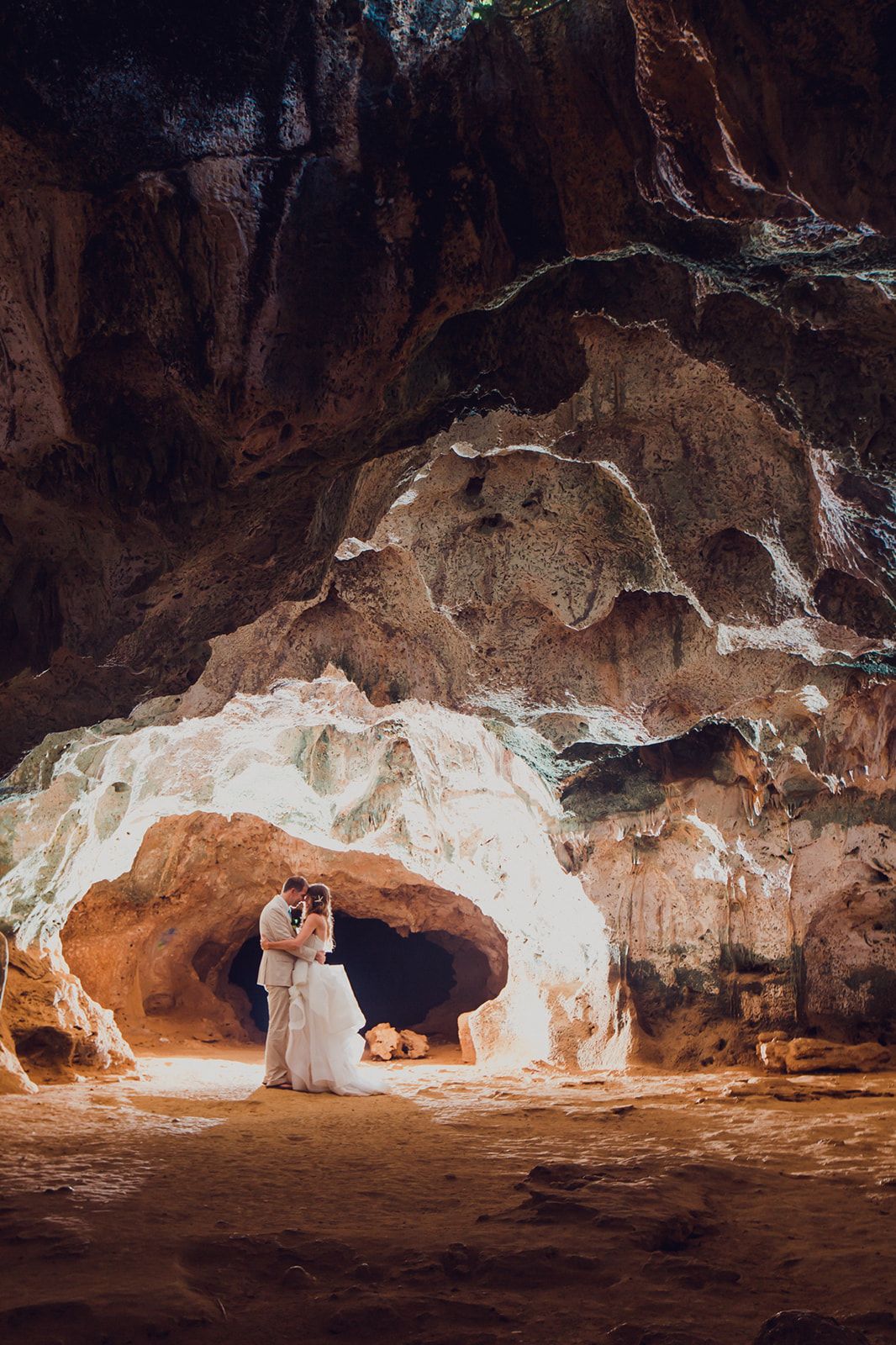Wedding couple silhouetted in dramatic cave setting with natural light streaming through.