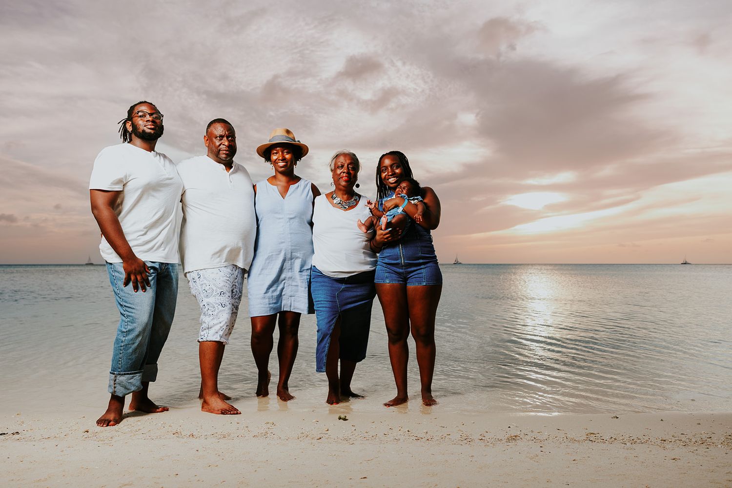 A group of people walking together on a sandy beach at sunset with calm ocean waters in the background.