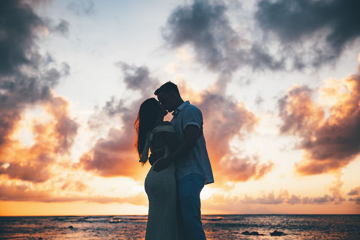 Romantic silhouettes of couple against dramatic sunset sky over ocean.