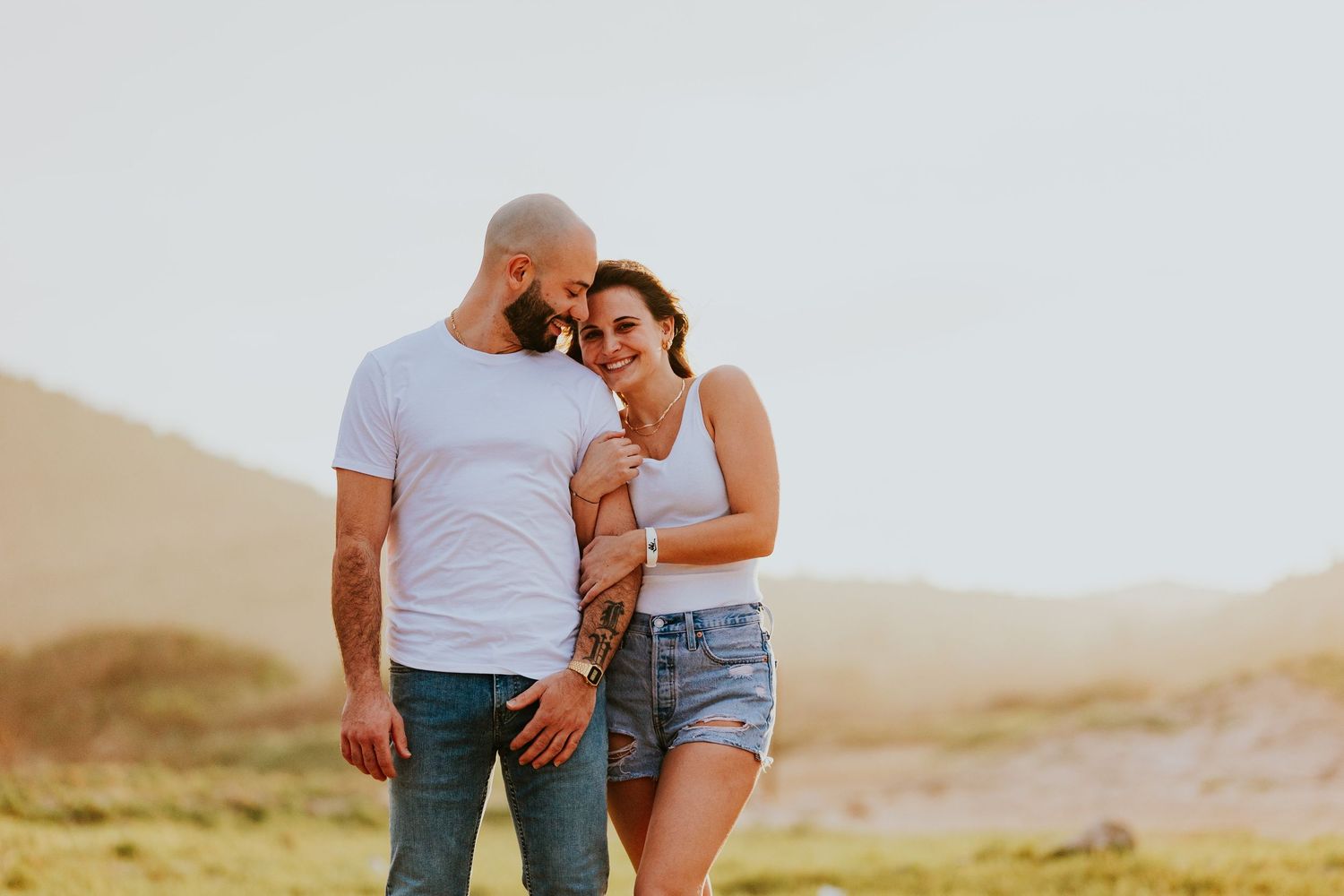 Couple embracing in casual outfits against desert landscape at golden hour.