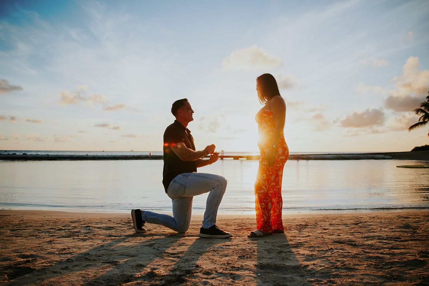 A romantic beach proposal silhouette at sunset with waves crashing in the background.