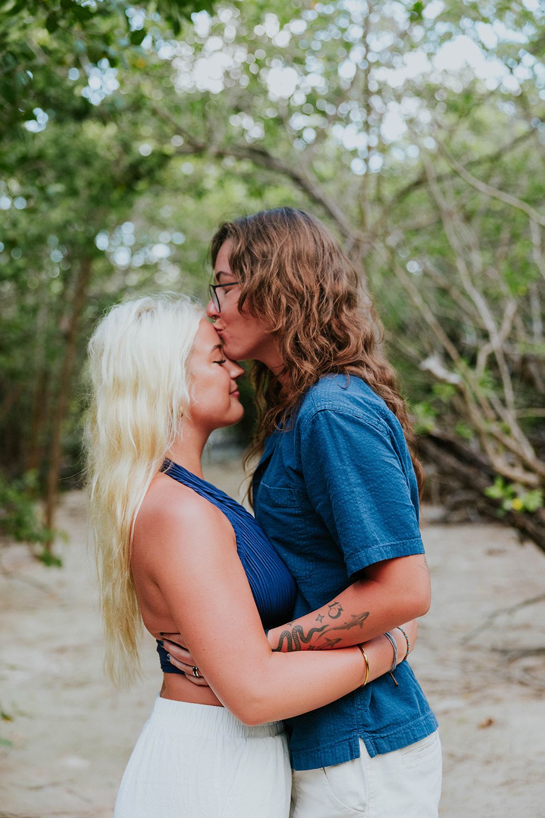 A romantic couple shares tender moments together in a natural outdoor setting with trees and greenery in the background.