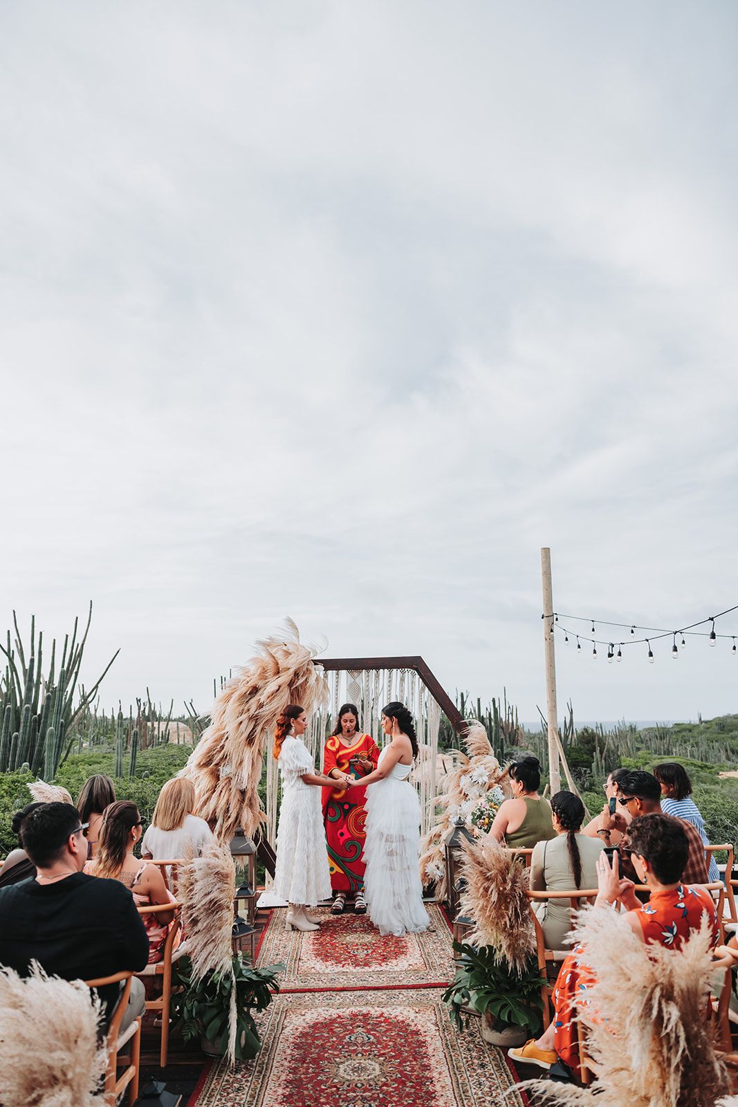 Boho desert wedding ceremony with pampas grass decorations and guests celebrating on a Persian rug aisle runner.