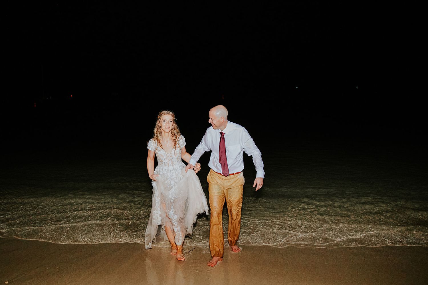 Silhouettes of people walking along a dark beach at night with their feet in the water.