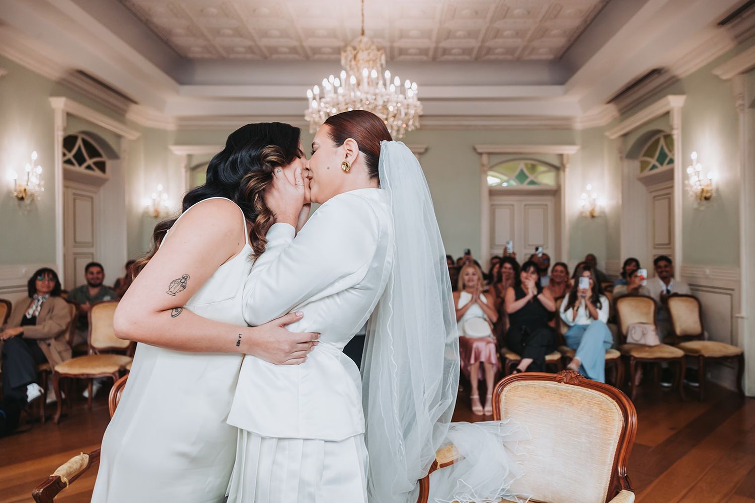 A romantic first dance moment captured in an elegant ballroom with a sparkling chandelier overhead.