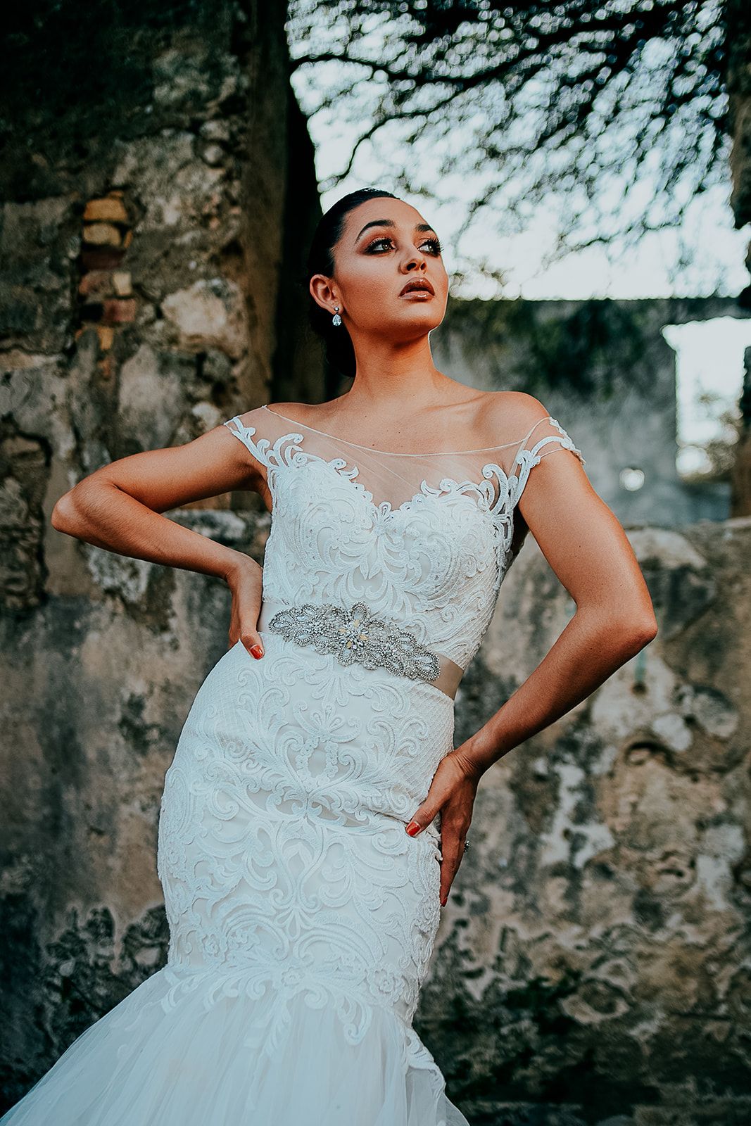 Stunning lace wedding dress with intricate embroidery details against stone wall backdrop.