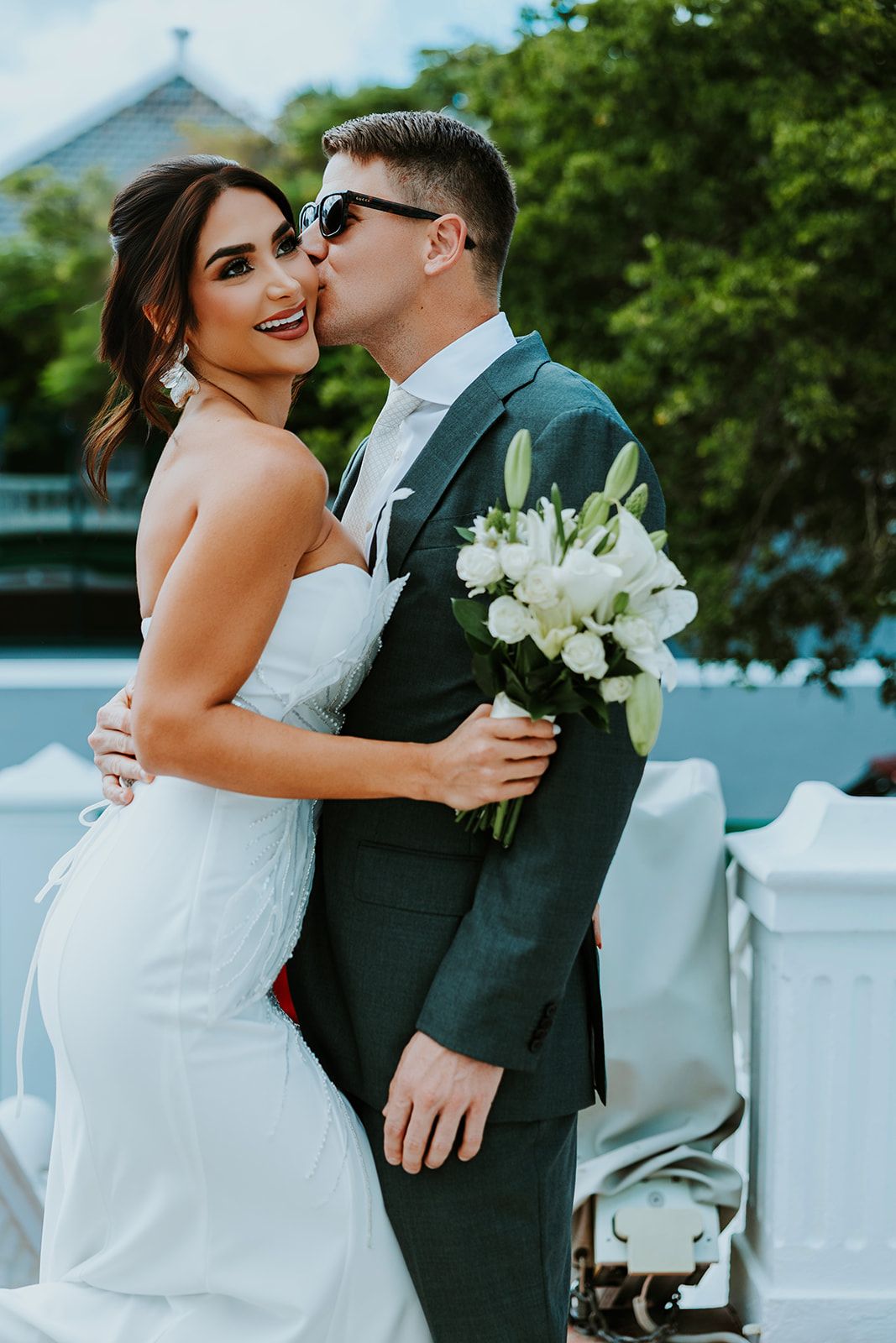A romantic wedding moment captured outdoors with white flowers and elegant attire against a green background.