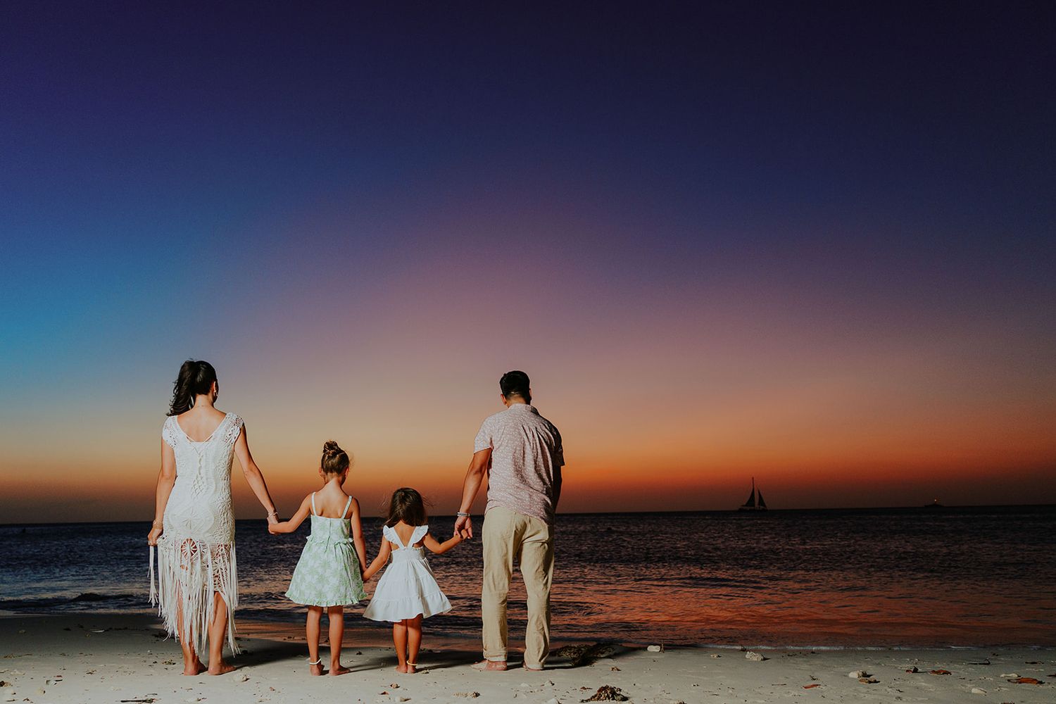 Silhouettes of a family holding hands while walking along a beach at sunset with vibrant orange and blue sky.